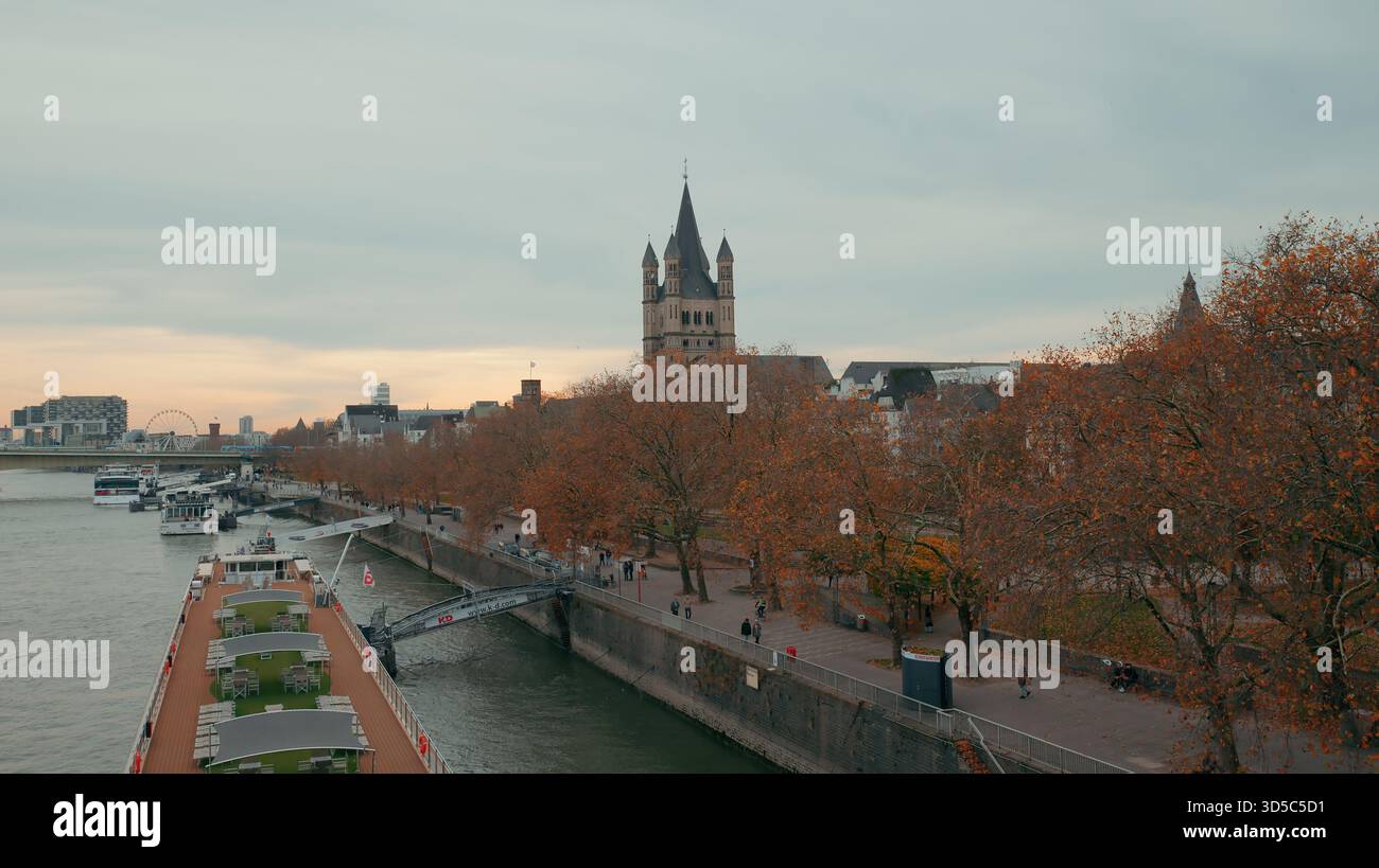 Les bateaux bordent une rivière paisible tandis que les gens se promènent le long du front de mer sous les arbres d'automne colorés au crépuscule. Banque D'Images