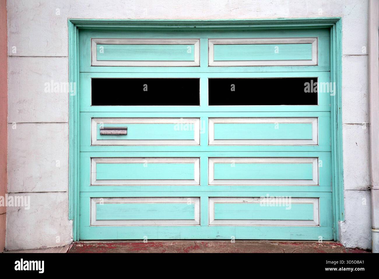 Porte de garage vert menthe pastel sur une maison de San Francisco, avec des panneaux géométriques simples et une tranche de mur rose doux Banque D'Images