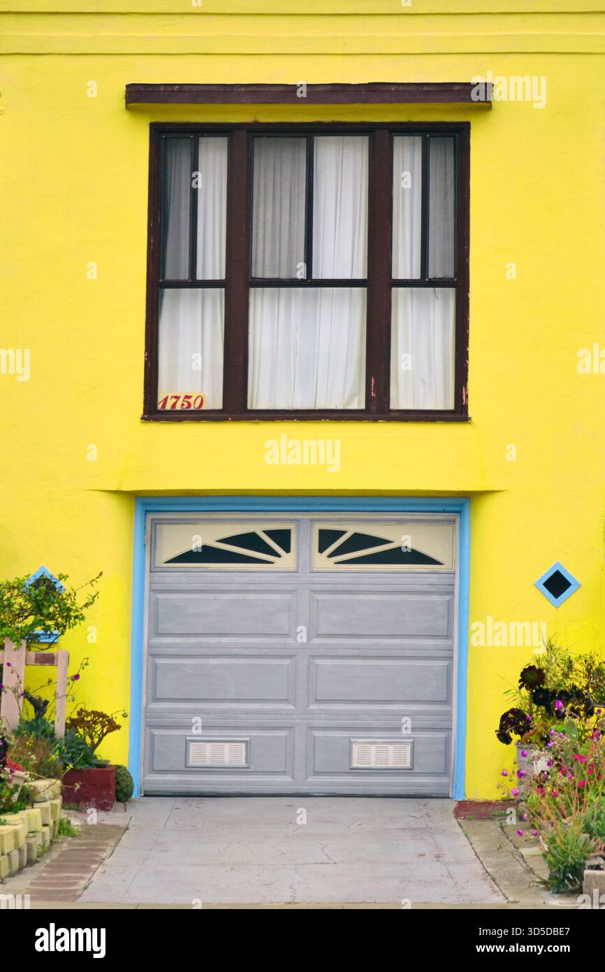 Extérieur coloré de la maison San Francisco avec porte de garage grise, murs jaune vif et plantes vibrantes le long de l'entrée Banque D'Images