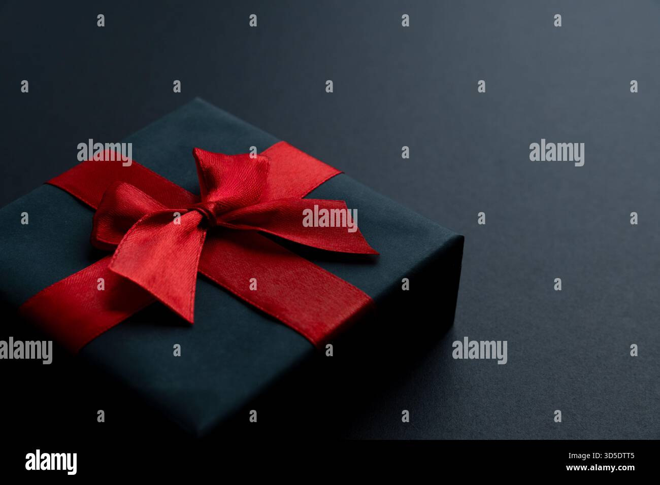 Un coffret cadeau noir avec un ruban de satin rouge vif et un noeud sur un fond noir. Mystère, élégance, soldes du Black Friday et cadeaux haut de gamme Banque D'Images