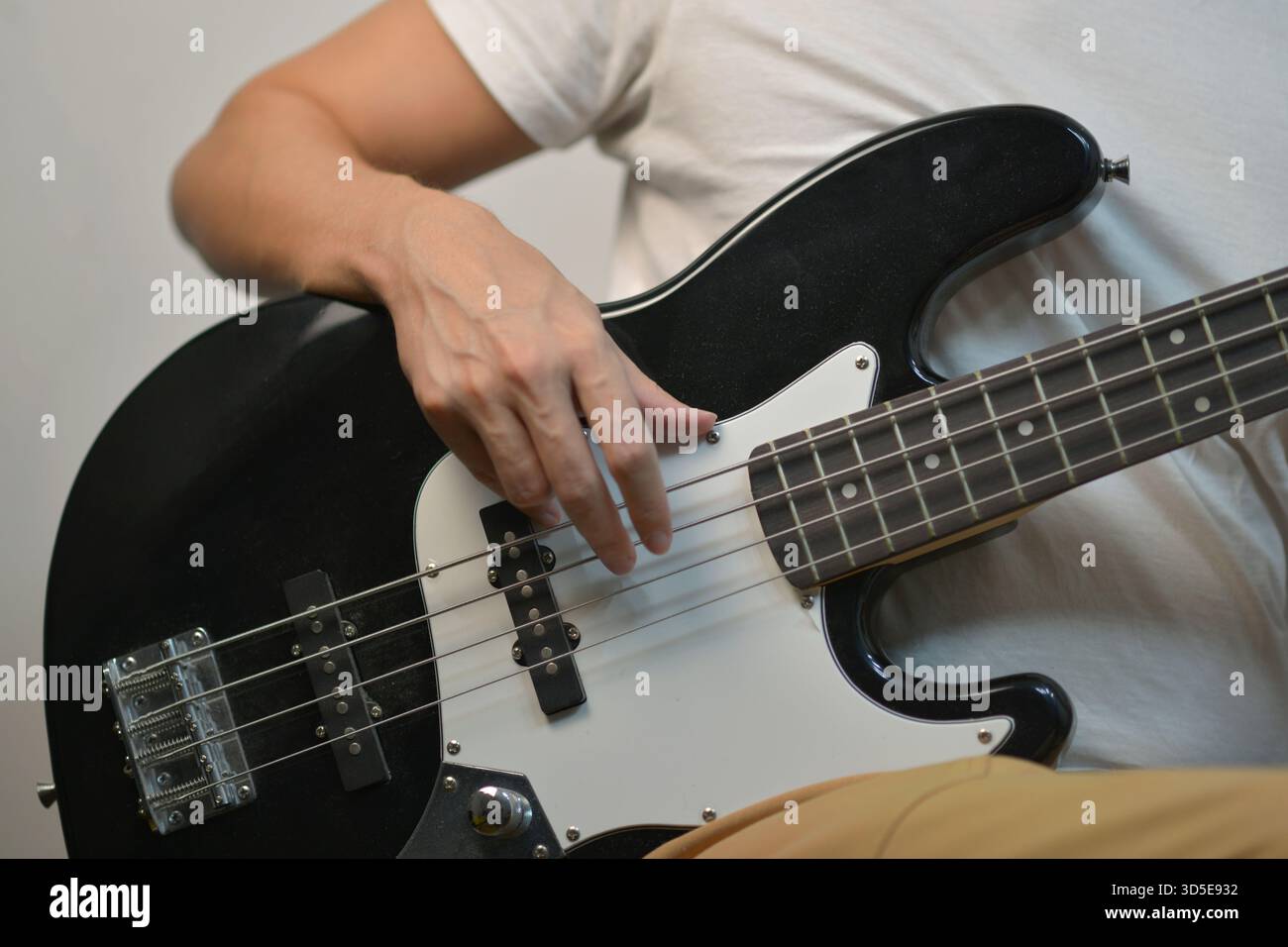Gros plan d'un homme arrachant les cordes d'une guitare basse électrique noire. Concentrez-vous sur la position de la main, les détails de l'instrument et la performance musicale. Banque D'Images