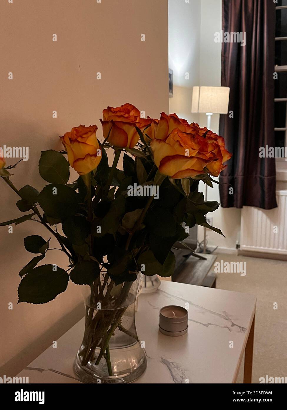 Un arrangement élégant de roses orange placées dans un vase en verre sur une table intérieure moderne à Hull, en Angleterre. - Image de stock capturée avec un smartphone