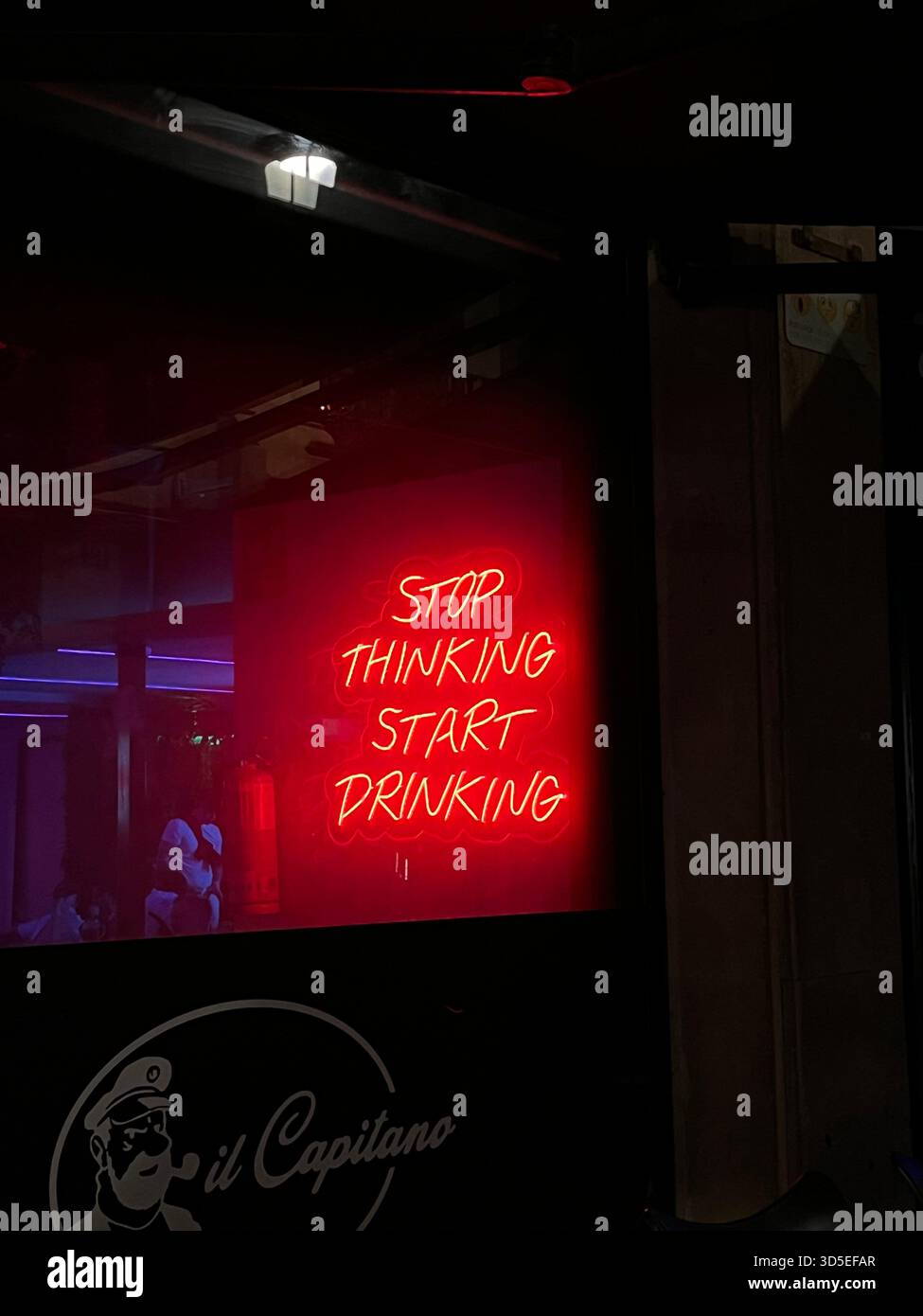 Un panneau rouge vif au néon lisant “Stop Thinking Start Drinking” affiché dans un lieu de vie nocturne à Alicante. L'éclairage audacieux crée une atmosphère animée Banque D'Images