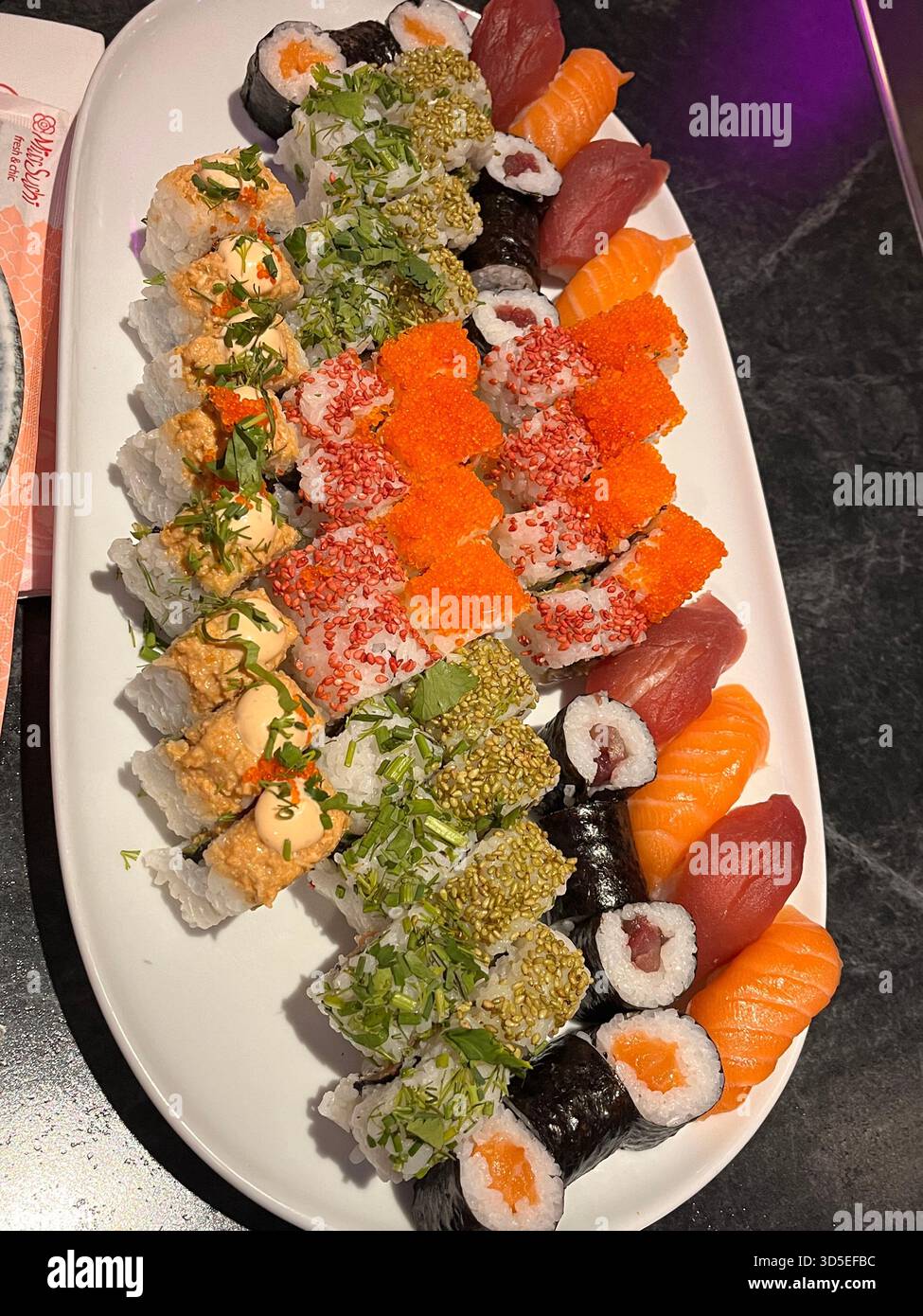 Un plateau de sushis magnifiquement arrangé avec des rouleaux vibrants, des sashimis et des garnitures servis sur un plat blanc. Capturé dans un restaurant à Alicante, Banque D'Images
