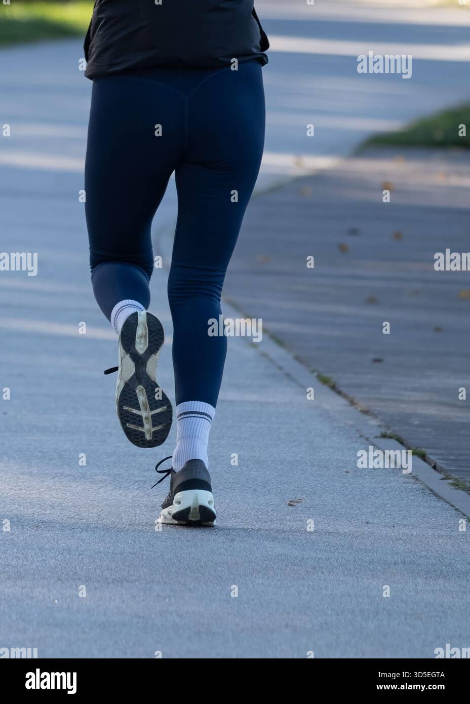 Vue arrière d'une personne marchant sur un chemin de parc pavé en vêtements de sport et chaussures de course. Concept de style de vie actif adapté au fitness, au bien-être, au par urbain Banque D'Images