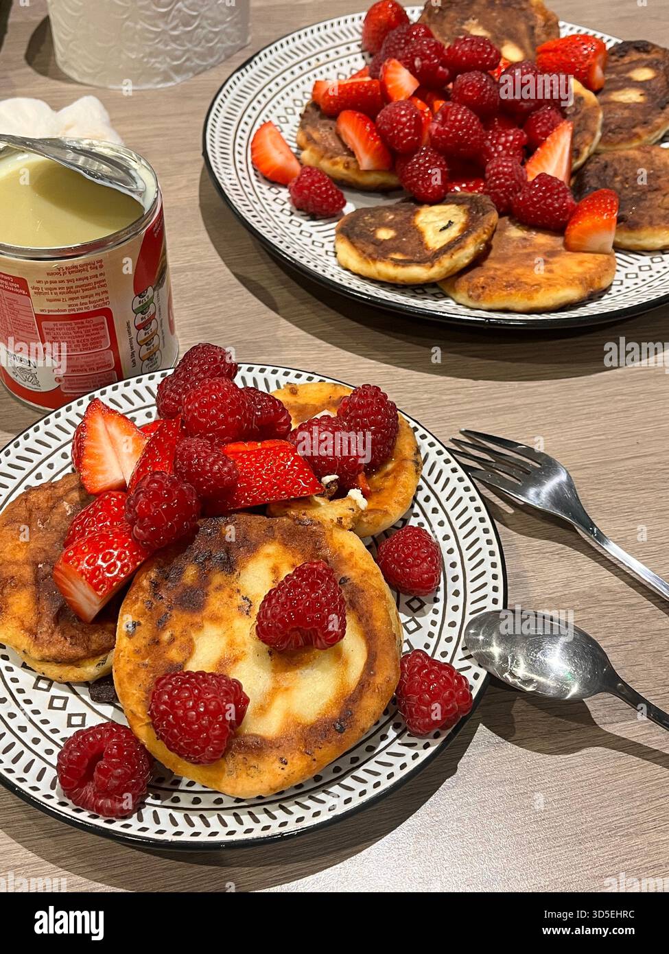 Une vue rapprochée de crêpes maison surmontées de fraises fraîches sur une assiette à motifs. Le petit déjeuner est posé sur une table en bois, - Image de stock capturée avec un smartphone