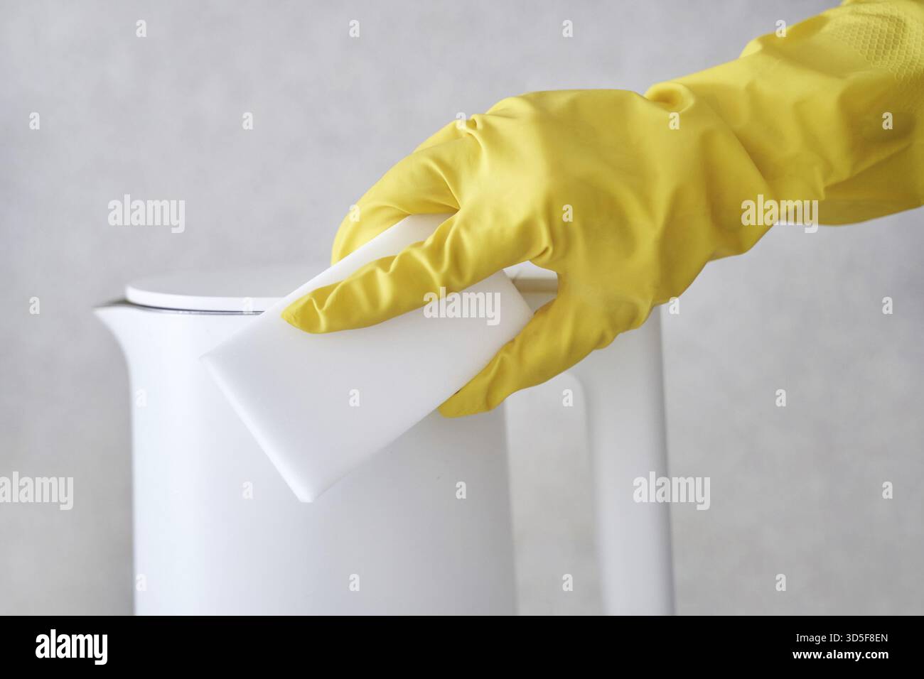 Personne nettoyant la bouilloire blanche avec un gant jaune et une éponge pour l'entretien et l'hygiène de la cuisine Banque D'Images