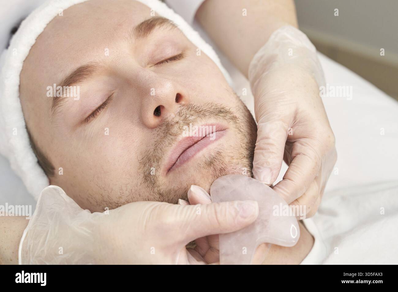 Docteur faisant la routine de la peau. Traitement de maternité en salon. Concept de soins de santé. Personne masculine. Massage facial d'acupunture pandémique de guasha. Procédé anti-âge Banque D'Images