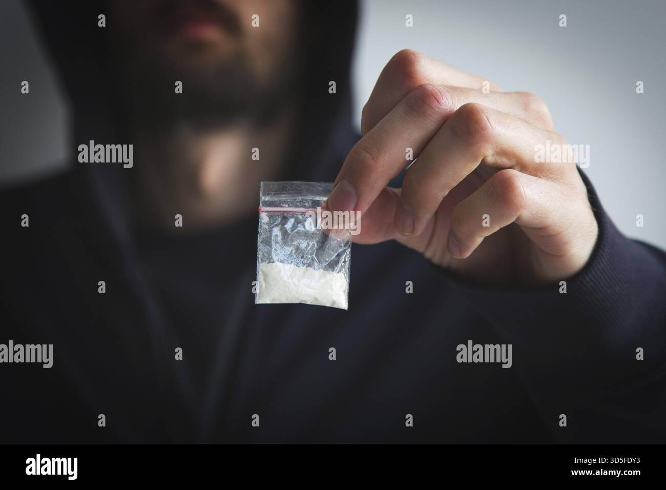 Homme en sweat-shirt et sweat à capuche sans visage tient un petit sac avec une substance blanche - drogue, concept de toxicomanie, dépendance et distribution Banque D'Images