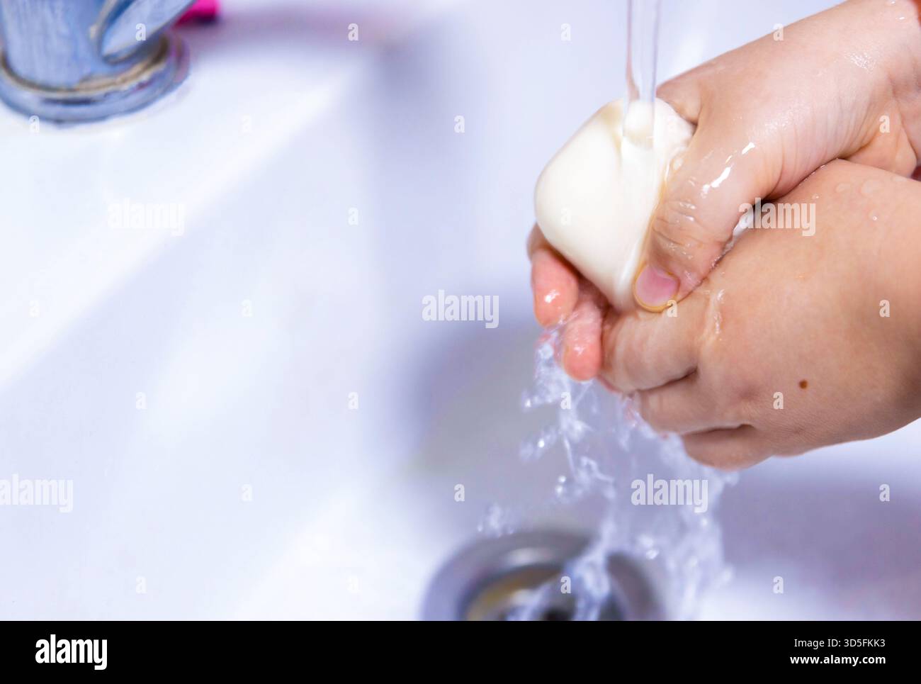 Les mains d'un enfant sont lavées avec du savon sous un robinet, soulignant l'importance de l'hygiène. Cette image met en évidence la pratique de l'ha propre Banque D'Images