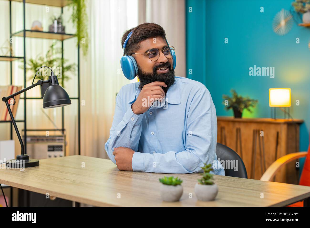 Homme indien à la maison assis portant des écouteurs déplace le corps au rythme de la musique ressent plaisir et liberté. Un homme arabe au bureau acquiert la tête garde le rythme partage le mouvement de danse souriant montrant l'énergie exciter une grande joie. Banque D'Images
