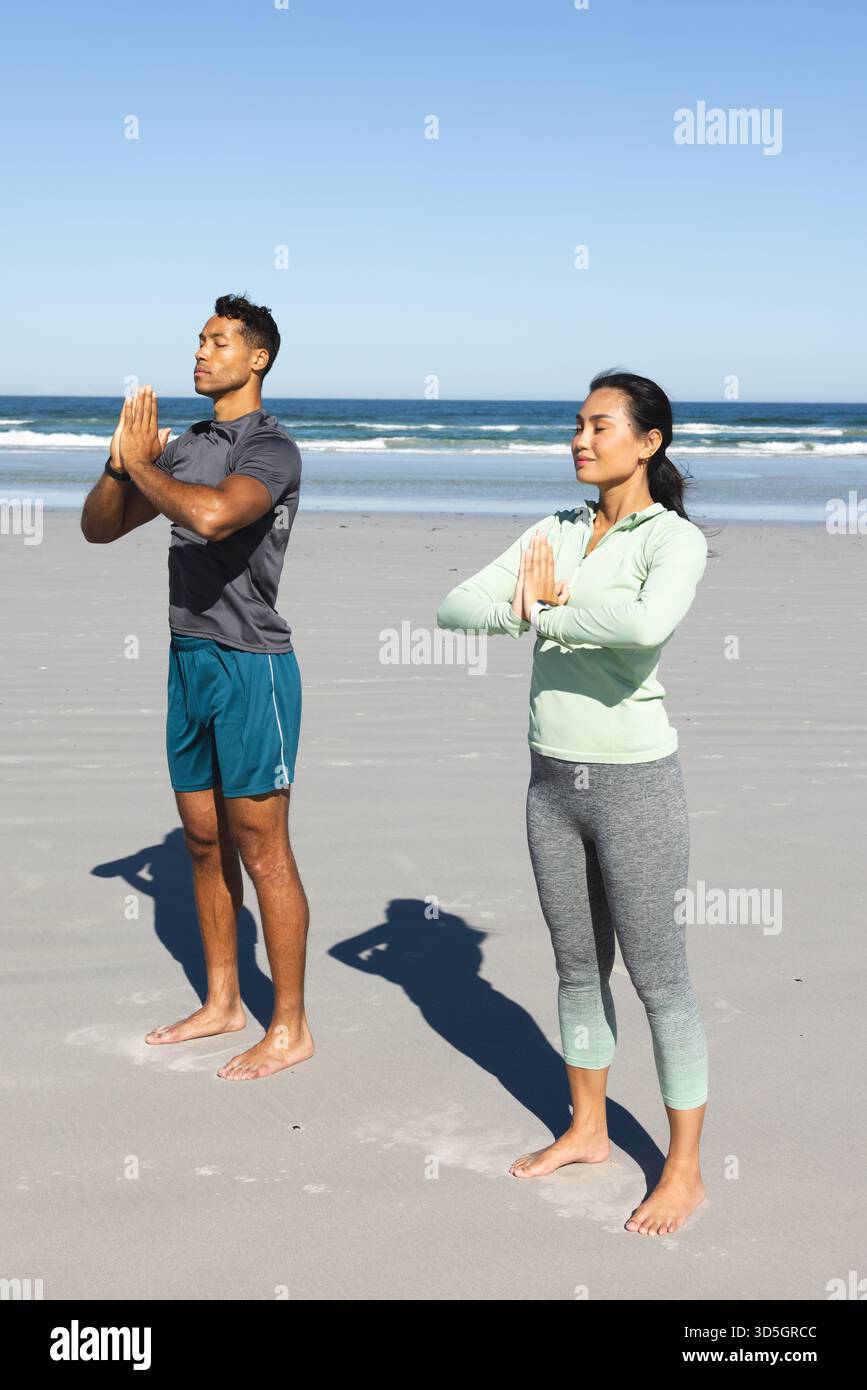 Couple pratiquant le yoga sur la plage, debout dans la pose de prière, profitant du soleil du matin Banque D'Images