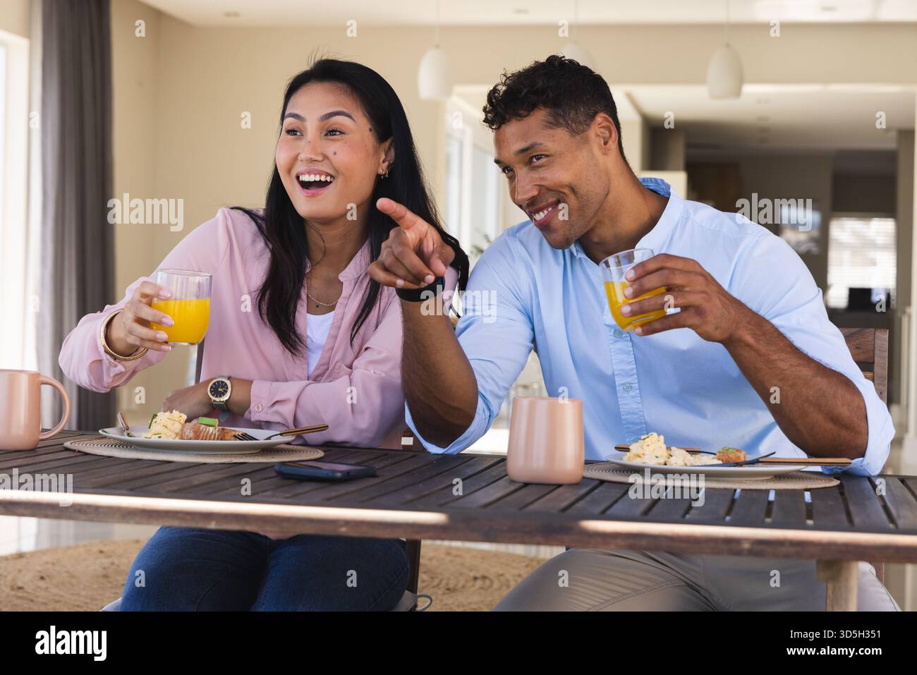 Couple appréciant le petit déjeuner ensemble, souriant et pointant tout en buvant du jus d'orange Banque D'Images