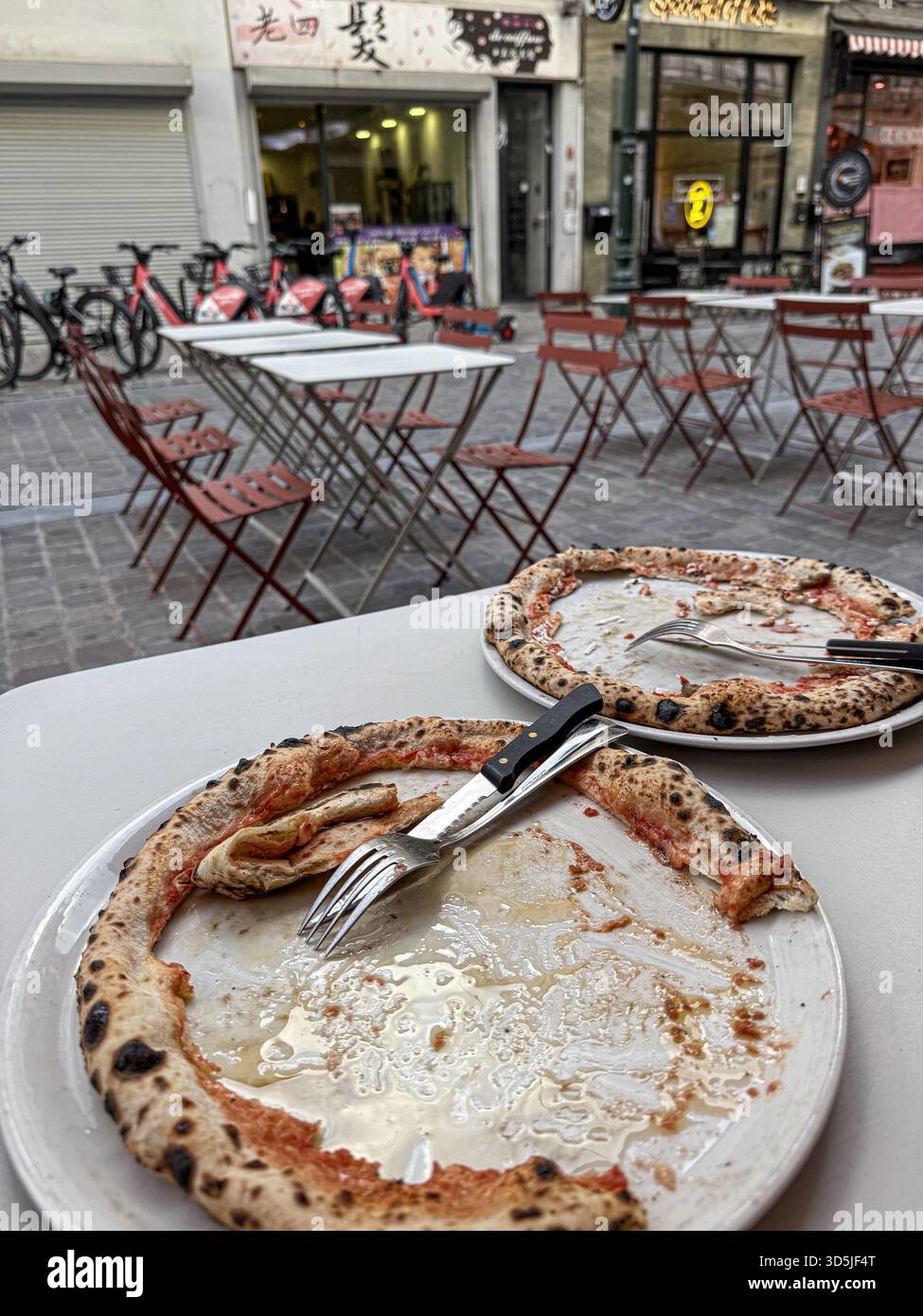 Deux assiettes de pizza vides avec des restes de croûtes et des couverts sont assis sur une table dans un restaurant en plein air Banque D'Images