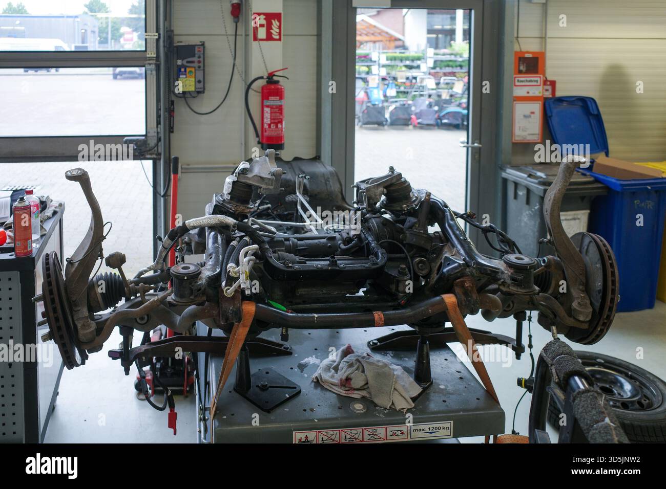 Une vue détaillée à l'intérieur d'un atelier de réparation automobile professionnel montrant un berceau avant de voiture avec suspension, direction et composants de transmission placés sur Banque D'Images