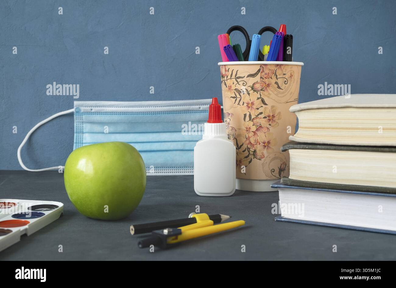 Livres, pomme et papeterie pour l'étude. Le masque médical comme symbole du covid-19 en arrière-plan. De retour à l'école, la protection contre l'infection est une conc Banque D'Images