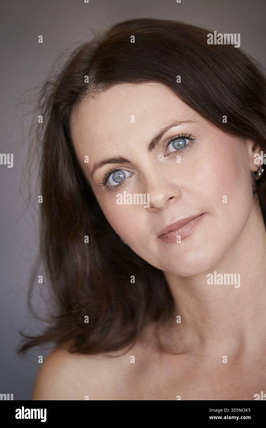 Portrait de femme avec les yeux bleus et les cheveux bruns sur fond gris doux Banque D'Images