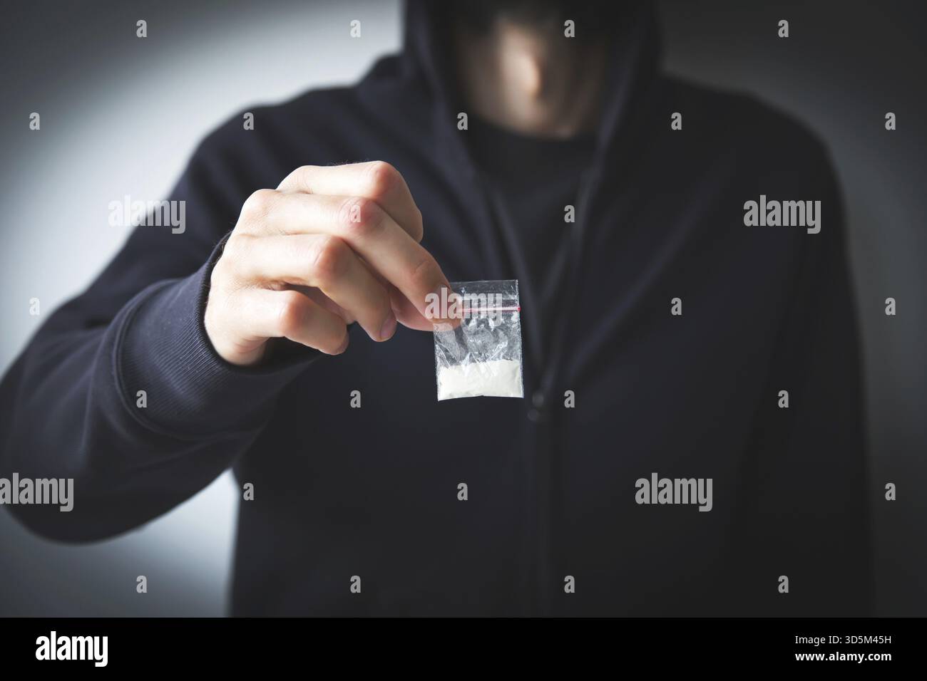 Homme en sweat-shirt et sweat à capuche sans visage tient un petit sac avec une substance blanche - drogue, concept de toxicomanie, dépendance et distribution Banque D'Images
