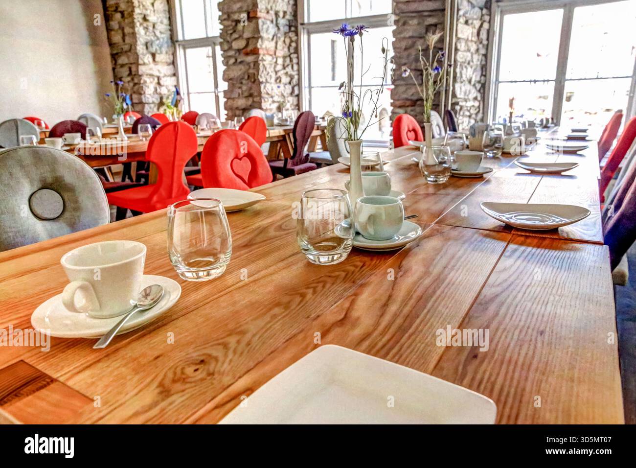 Intérieur coloré du restaurant à Tallinn avec tables, chaises vibrantes et murs en pierre éclairés par de grandes fenêtres. Banque D'Images
