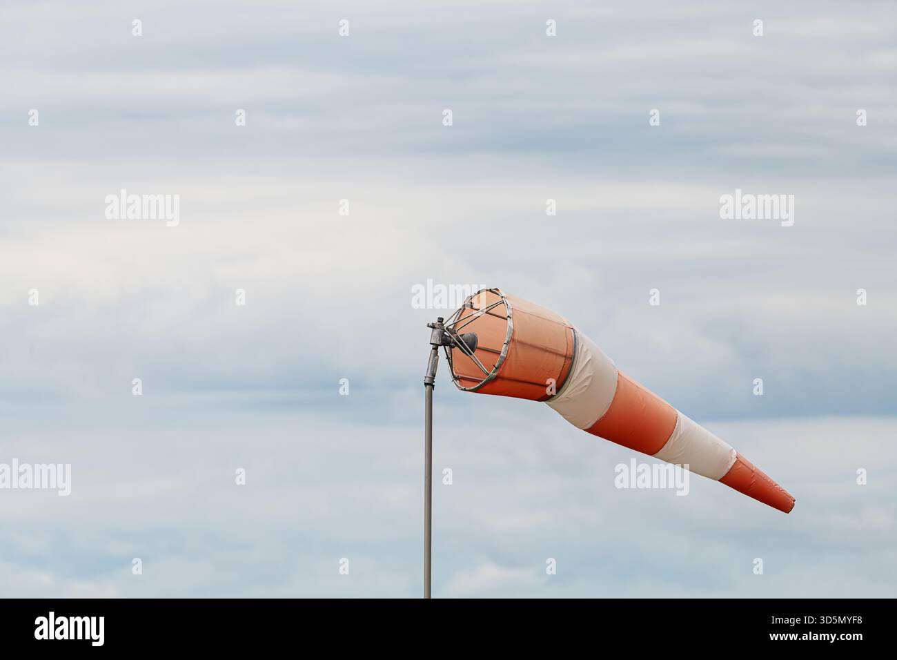 Chaussette horizontale rayée orange et blanche sur poteau métallique soufflant dans le vent contre ciel nuageux couvert. Prise de vue sous un angle bas montrant la direction du vent ind Banque D'Images