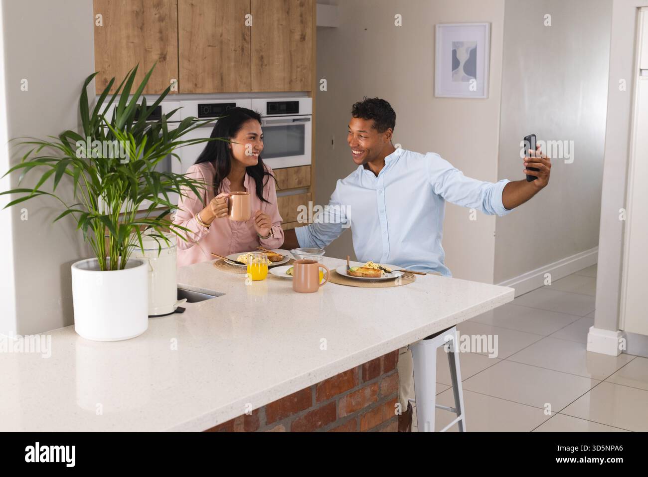 Couple appréciant le petit déjeuner à la maison, prenant selfie avec smartphone, souriant joyeusement Banque D'Images