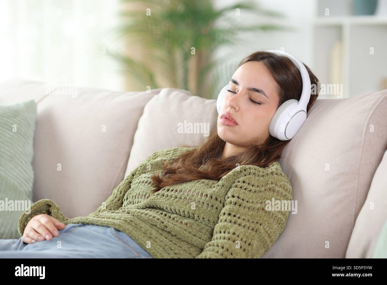 Femme en vert portant casque dormant assis sur un canapé à la maison Banque D'Images