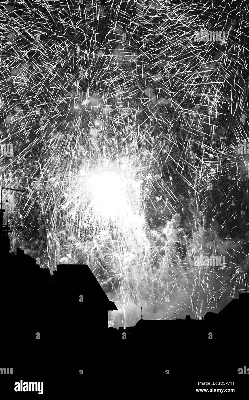 Feux d'artifice colorés explosant dans le ciel nocturne au-dessus de bâtiments silhouettes. Banque D'Images