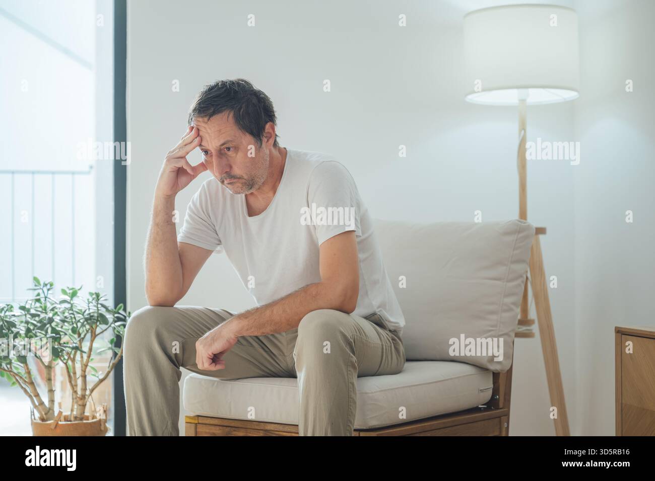 Portrait de triste homme déprimé assis seul dans le salon, regardant vers le bas avec regret et douleur émotionnelle dans un environnement domestique calme et faible luminosité. Sélectif Banque D'Images