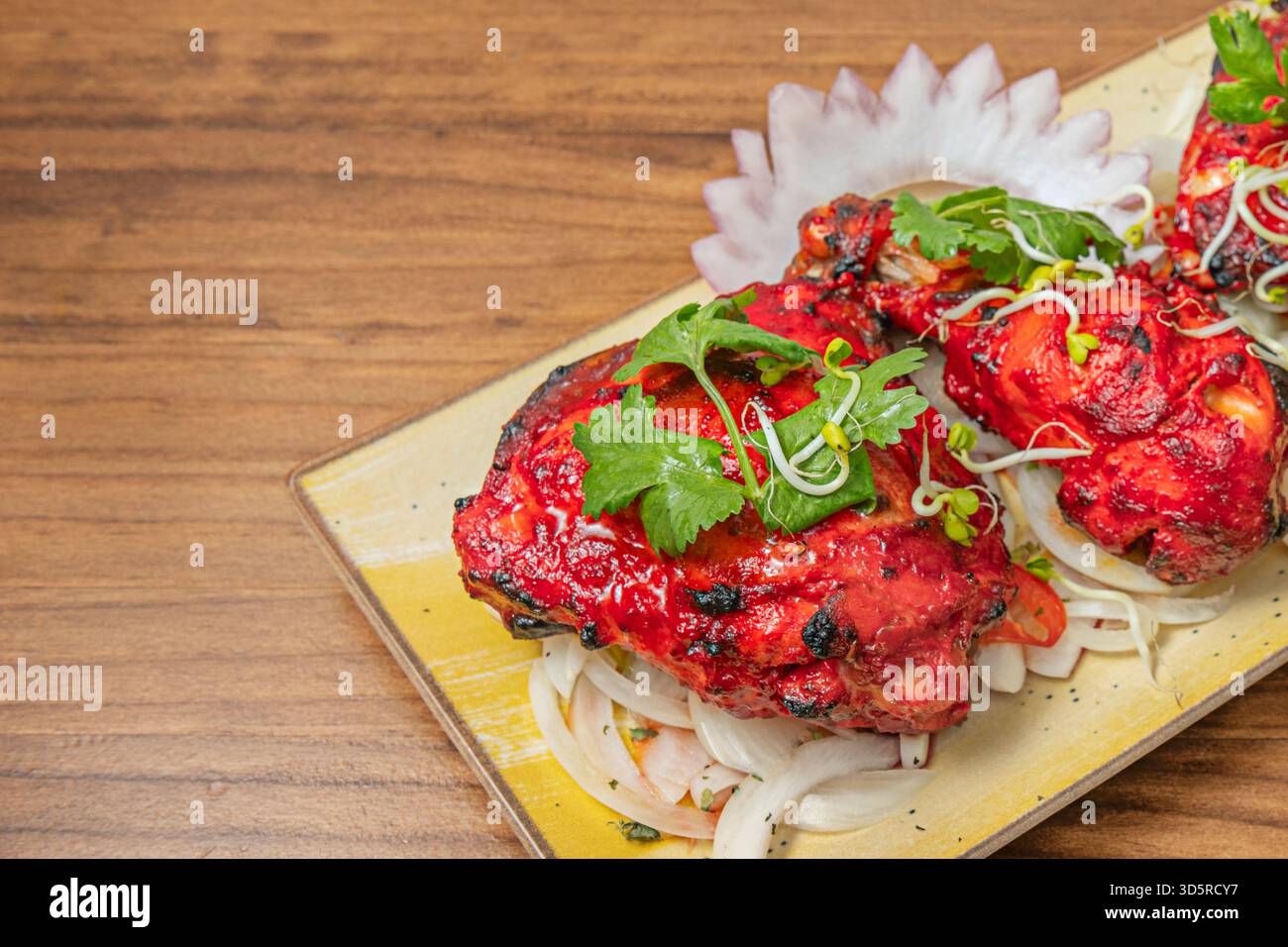 Un gros plan détaillé révèle la texture légèrement carbonisée et les herbes accrochées à la peau du poulet Tandoori fraîchement cuit. Banque D'Images
