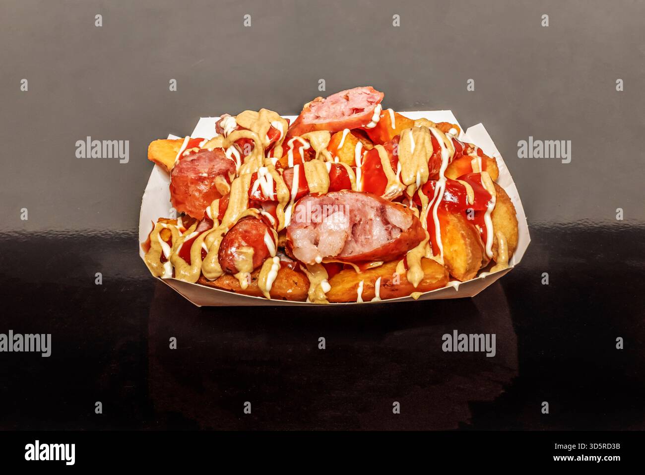 La combinaison classique de saucisses de porc grillées et de frites maison est servie sur un plateau en bois avec des lignes de moutarde et de mayonnaise maison Banque D'Images