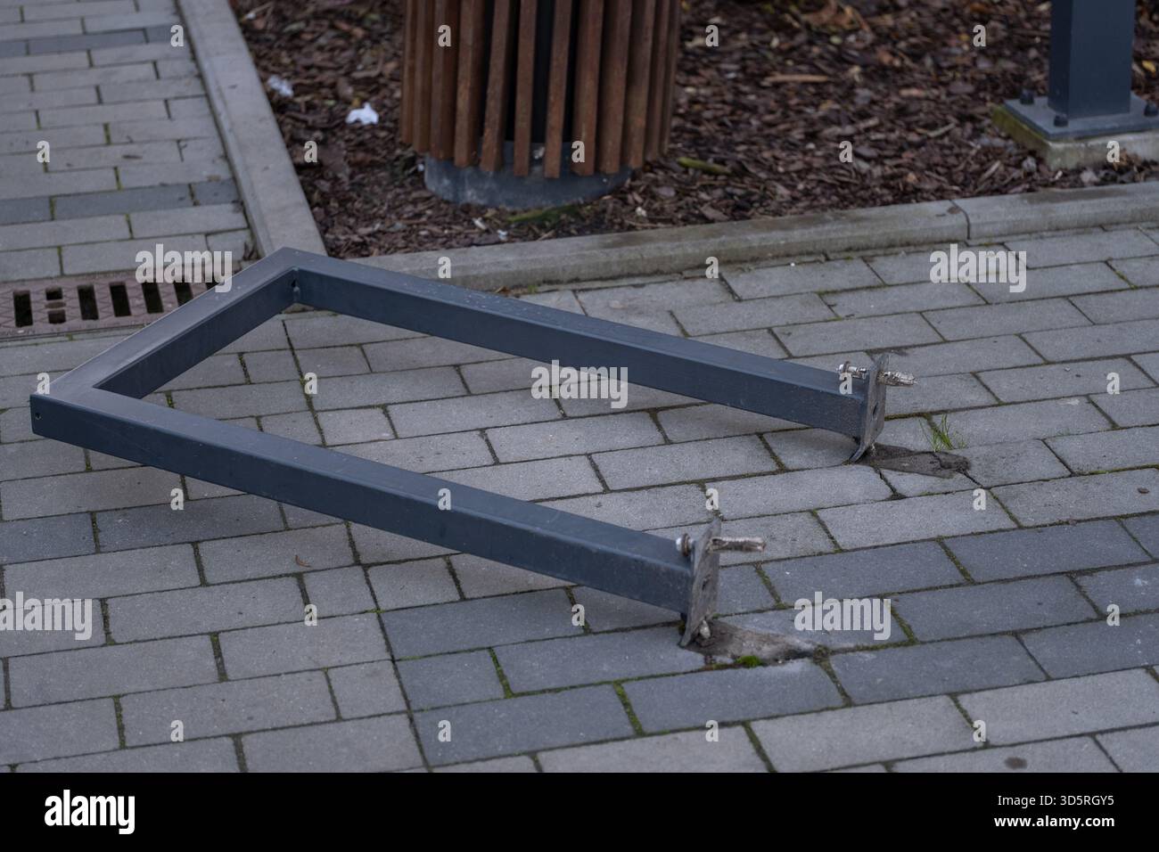 Un porte-vélos en métal endommagé reposant sur une passerelle pavée, avec des boulons exposés sur le sol. La scène montre l'infrastructure urbaine en mauvais état, adapté pour Banque D'Images
