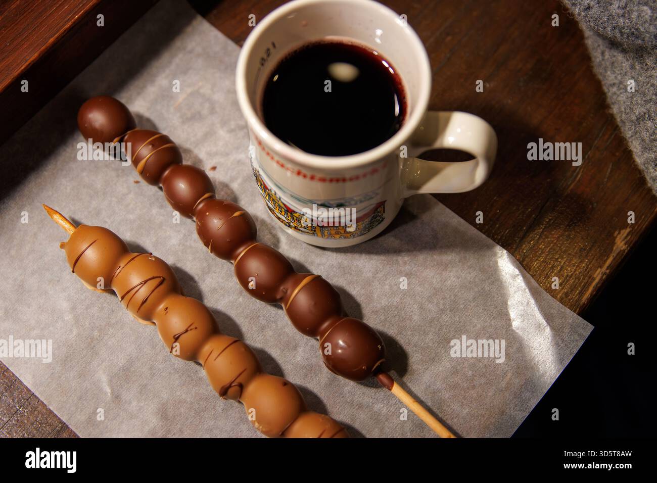 Würzburg, Allemagne, 23 décembre 2024. Brochettes recouvertes de chocolat à côté d'une boisson chaude sombre dans une tasse en céramique avec du vin chaud rouge sur la table du café à Banque D'Images