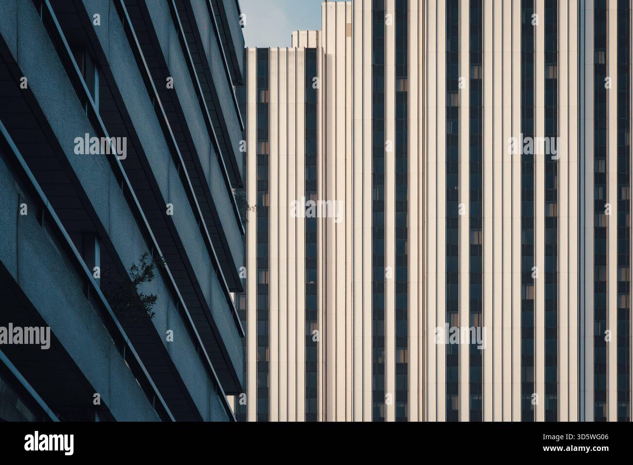 Photographie architecturale abstraite montrant le contraste géométrique entre la façade en verre diagonale et les lignes verticales du bâtiment dans les tons bleu-gris et beige Banque D'Images