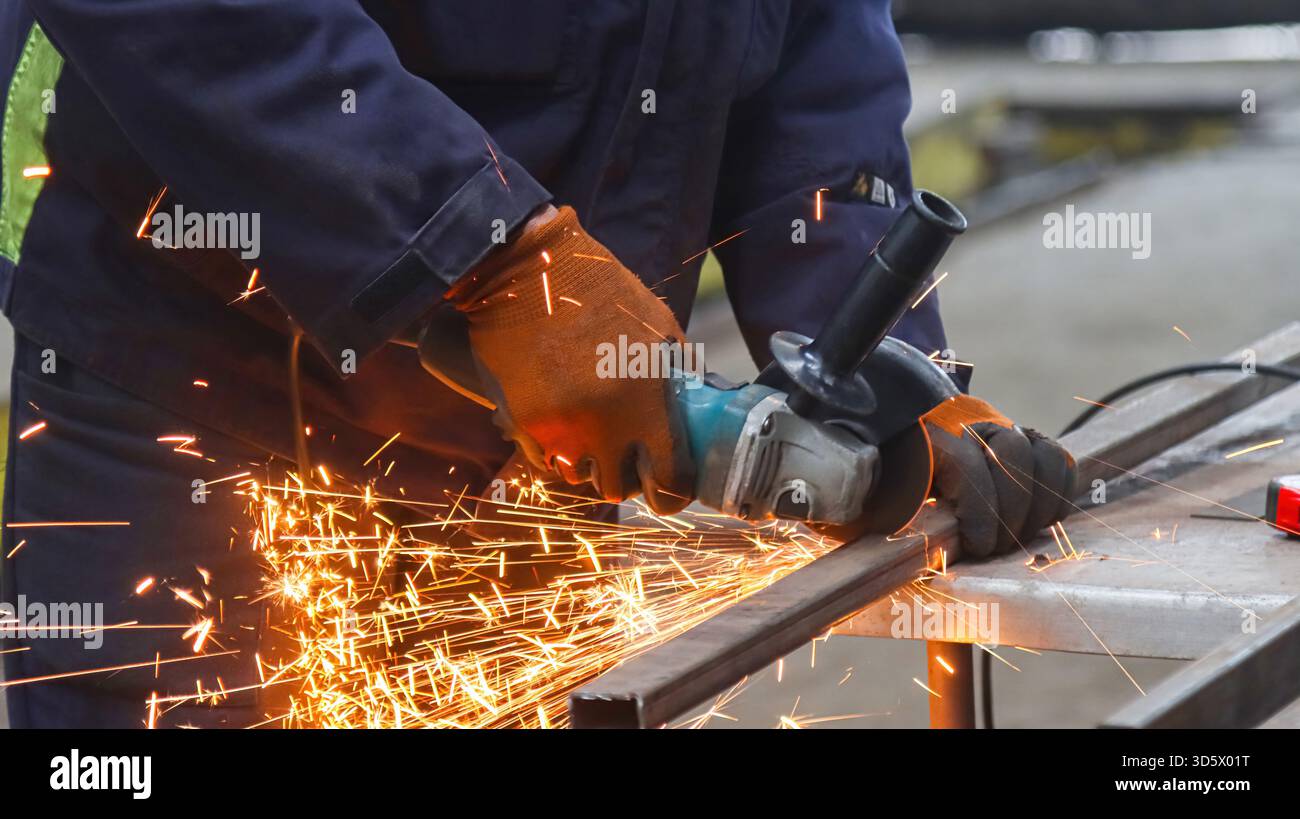 Un ouvrier coupe une poutre en acier avec une meuleuse d'angle. Banque D'Images