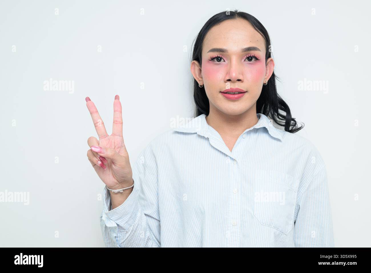 Portrait studio d'un jeune transgenre thaïlandais avec maquillage et cheveux longs. Concept d'expression de genre, fierté LGBTQ et inclusivité montrant un Banque D'Images