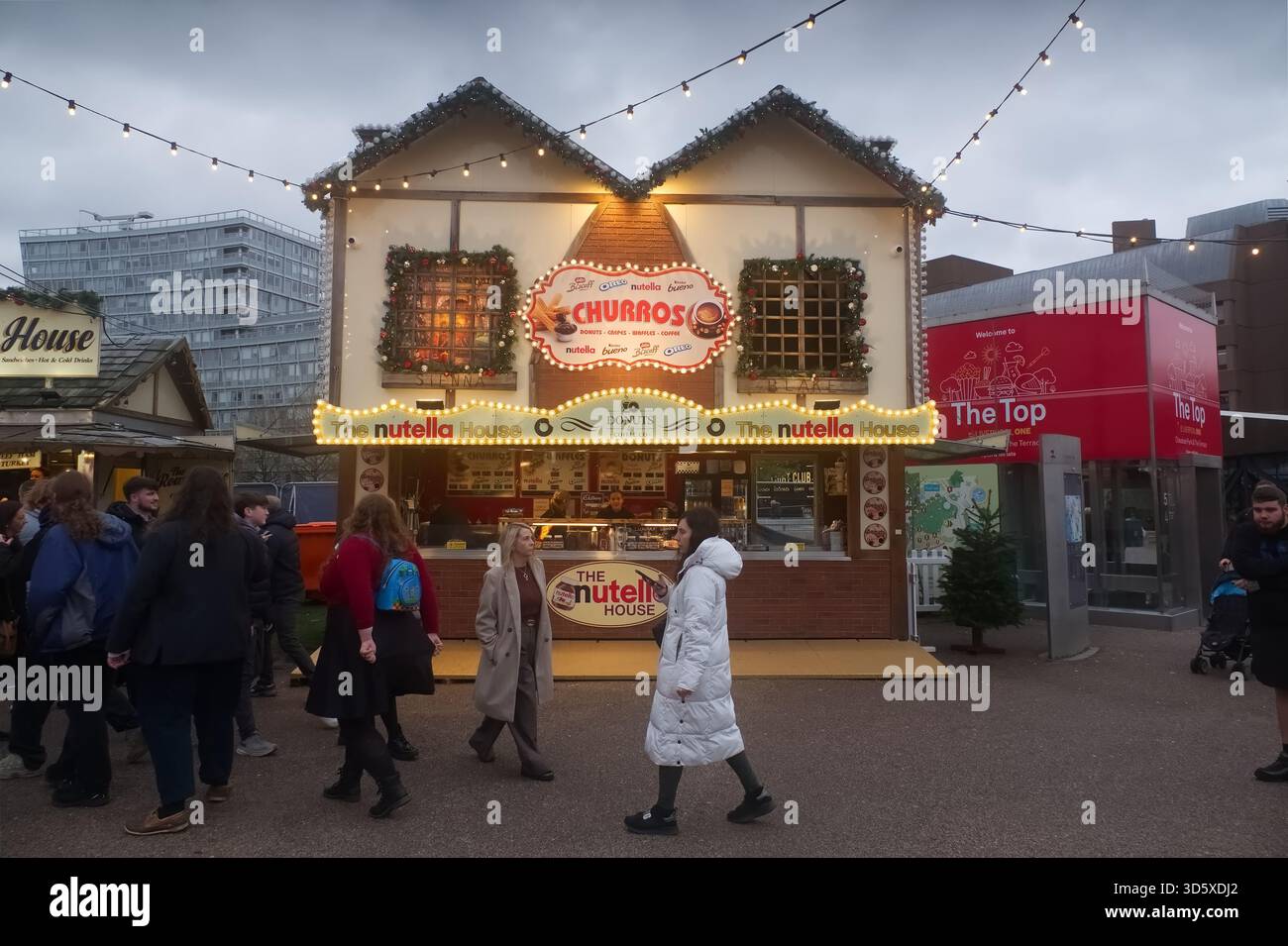 La maison Nutella et Churros Stand au marché de Noël Liverpool One, illuminés par des lumières festives au crépuscule avec les visiteurs qui passent devant. Banque D'Images