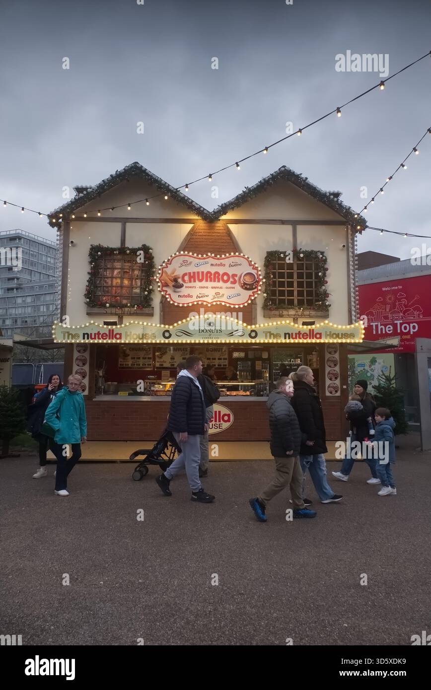 La maison Nutella et Churros Stand au marché de Noël Liverpool One, illuminés par des lumières festives au crépuscule avec les visiteurs qui passent devant. Banque D'Images