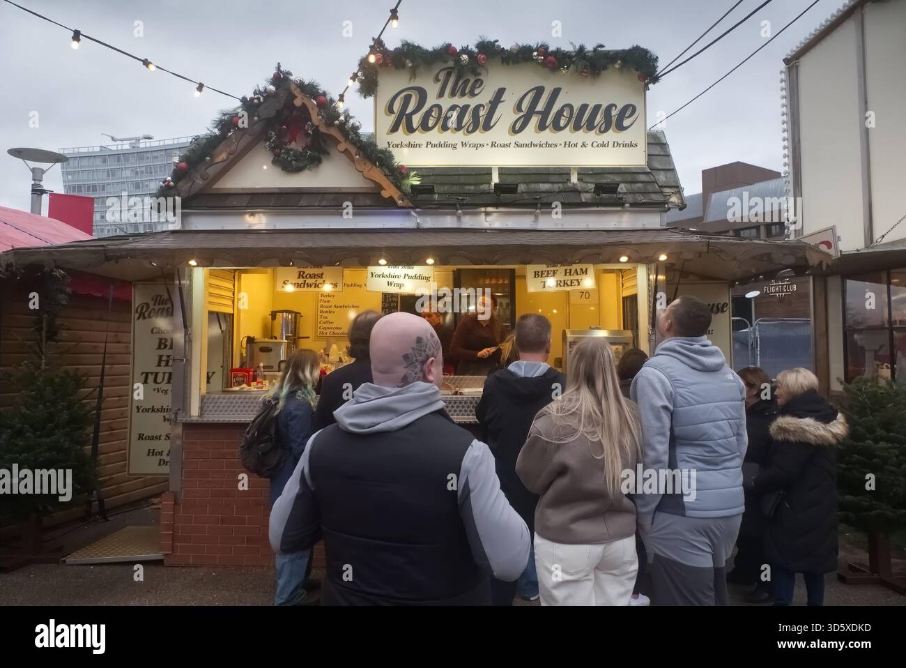 Les gens font la queue au stand « The Roast House » dans un marché de Noël de Liverpool One, vendant des wraps festifs Yorkshire Pudding et illuminés au crépuscule. Banque D'Images