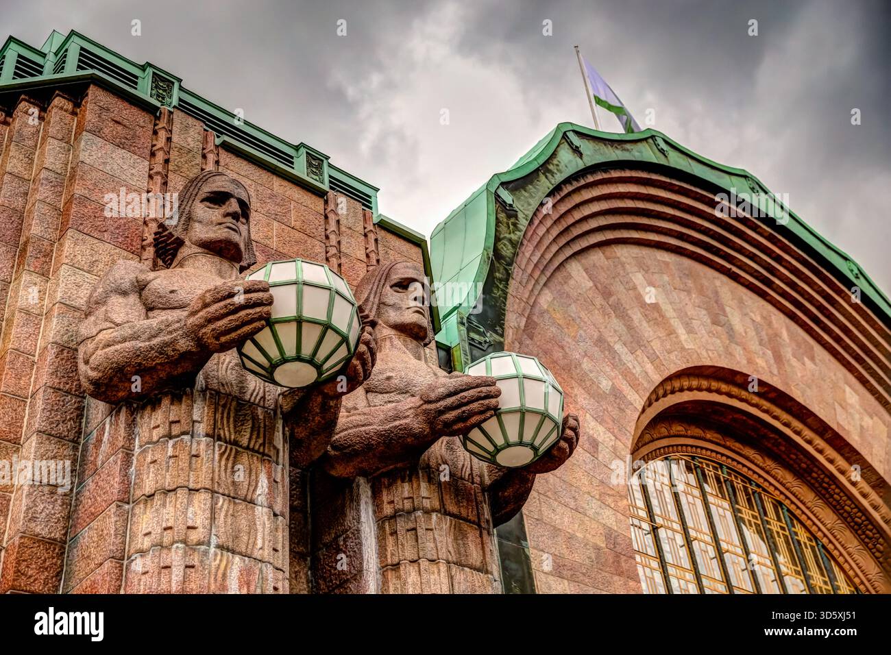 Façade avant de la gare centrale d'Helsinki avec son entrée voûtée, son horloge et ses figures emblématiques en pierre sous un ciel nuageux. Banque D'Images