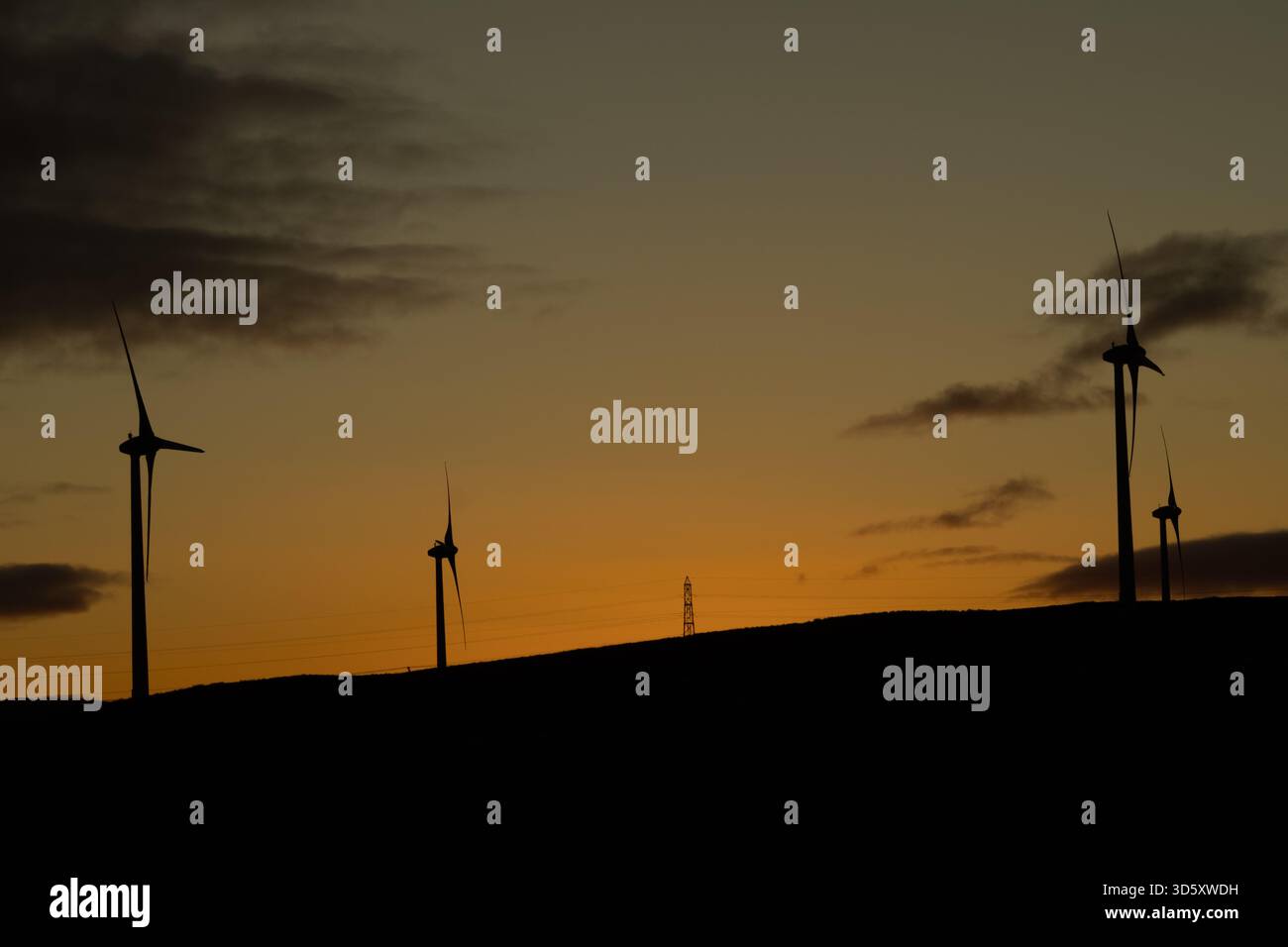 Les éoliennes silhouettes se dressent face à un coucher de soleil orange et brun vif, avec des nuages spectaculaires rehaussant la scène crépusculaire. Banque D'Images