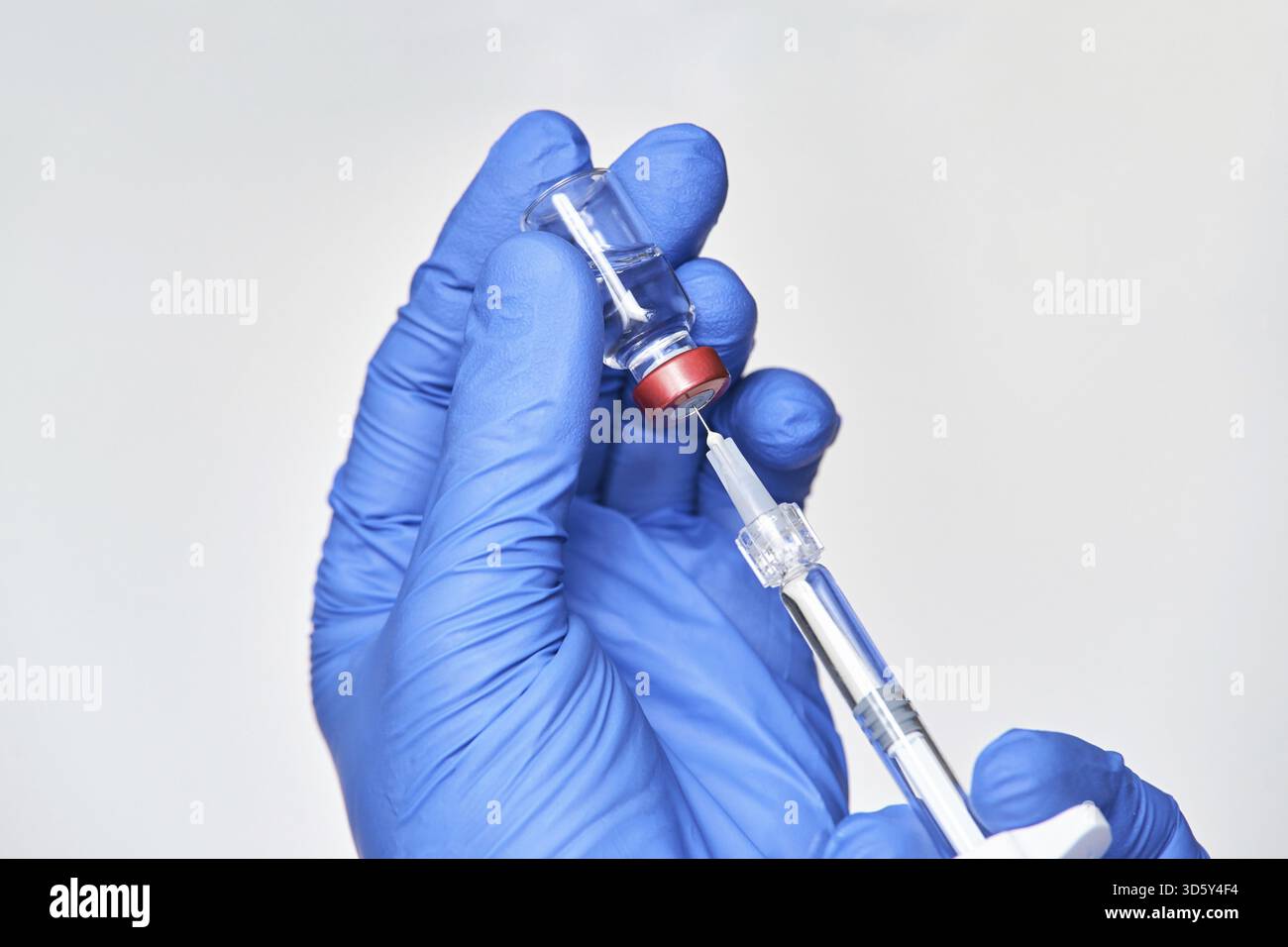 Médecin tenant le flacon avec injection dans les mains de gants bleus. Concept de grippe de laboratoire de pharmacie. Flacon en verre pour seringue vitaminique. Le traitement infirmier en médecine. Beaut Banque D'Images