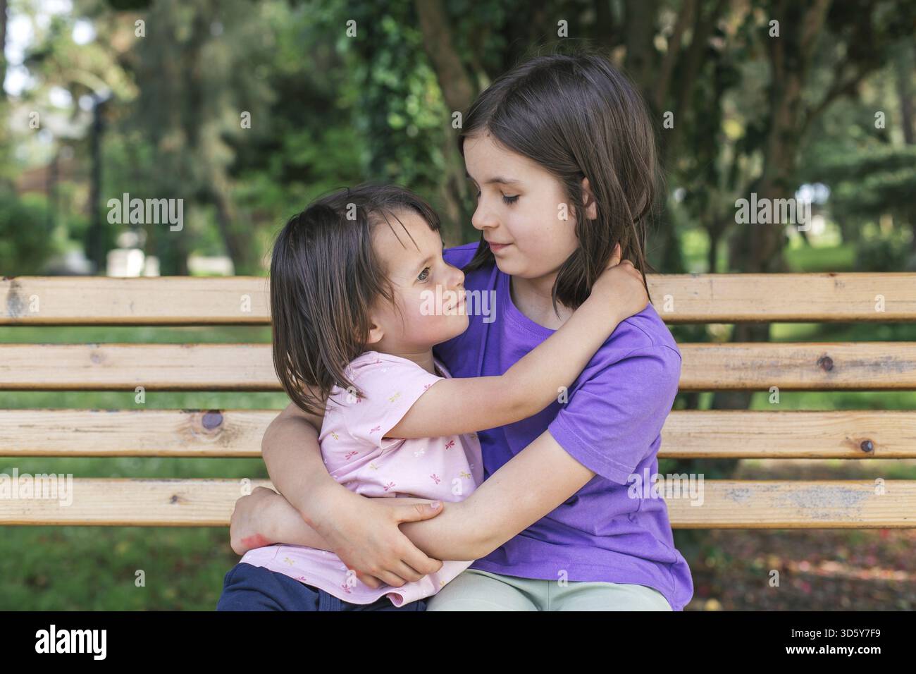 Deux filles enfants sœurs embrassant tout en étant assis sur un banc dans un parc, se regardant avec affection et tendresse Banque D'Images