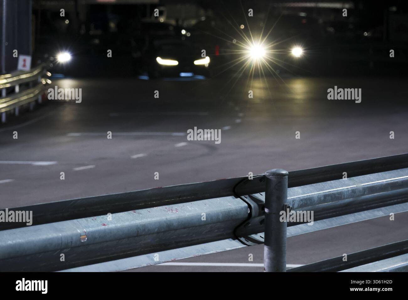 Deux voitures avec des phares brillants sur route sombre la nuit. garde-corps en métal au premier plan du garage de stationnement crée une scène suspensive mystérieuse et urbaine Banque D'Images