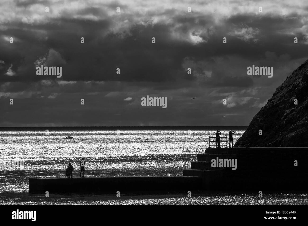 Vue côtière monotone avec des figures sur une jetée et de l'eau chatoyante Banque D'Images