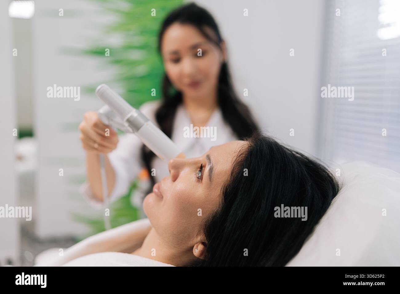 Gros plan d'une femme adulte obtenant une procédure esthétique non chirurgicale, cosmétologue appliquant un appareil à ultrasons sur le visage, stimulant le produit de collagène Banque D'Images