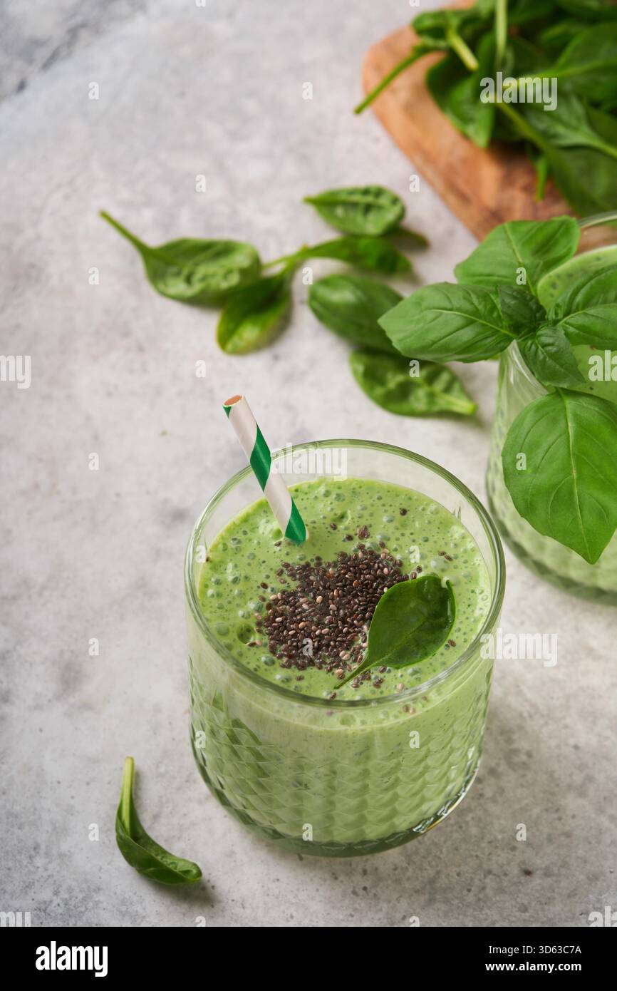 Smoothie aux épinards vert sain. Smoothie végétalien ou milkshake à partir d'épinards, de bananes et de graines de chia sur fond de table en béton gris. Manger propre, régime alcalin. Vue de dessus. Maquette. Banque D'Images