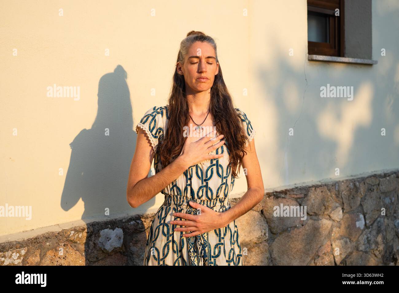 Femme mature méditant les yeux fermés, les mains sur la poitrine et le ventre, profitant d'un moment de pleine conscience à l'extérieur Banque D'Images