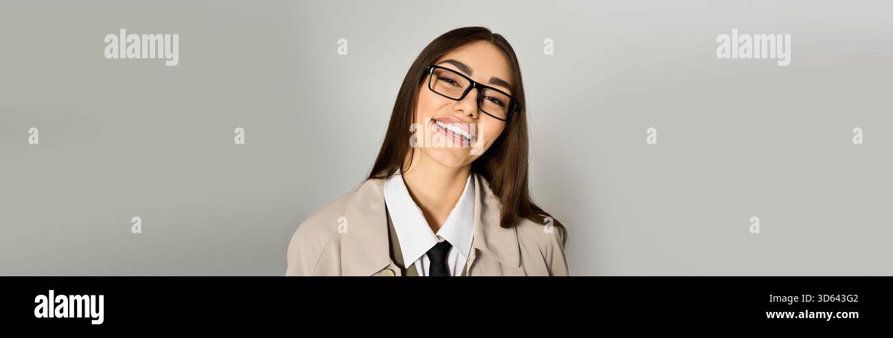 Une jeune femme heureuse pose avec un sourire amical, vêtue d'une tenue chic dans un cadre neutre. Banque D'Images