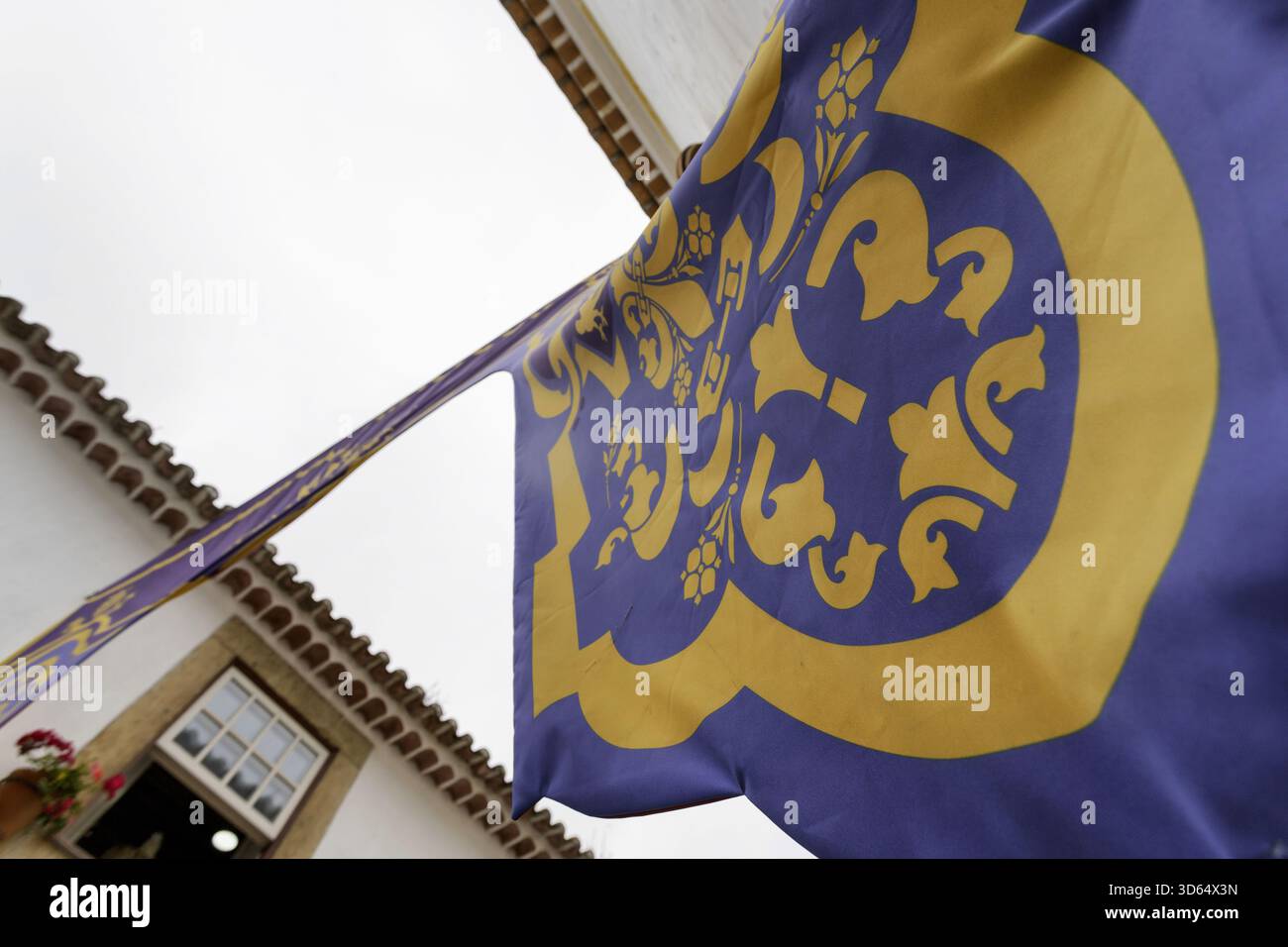 Vue d'une bannière bleue et jaune avec des motifs complexes flottant contre un bâtiment blanc avec des toits de tuiles rouges, projetant une scène vibrante, Obidos, Lei Banque D'Images