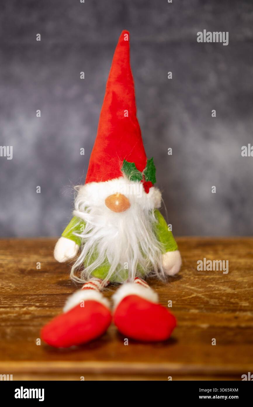 Gnome de Noël avec chapeau rouge reposant sur une base en bois et un fond sombre Banque D'Images